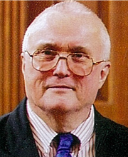 headshot photo of Dr. Charles Cox wearing dark blazer, striped button down shirt and blue tie
