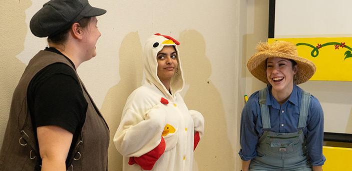 2 students playing farmers stand laughing on either side of a student playing a chicken